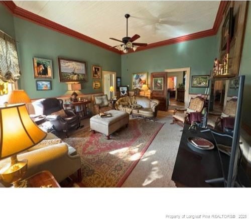 living area featuring lofted ceiling, carpet, ornamental molding, and a ceiling fan