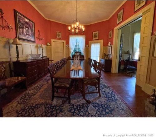 dining room with a wainscoted wall, crown molding, a decorative wall, an inviting chandelier, and wood finished floors