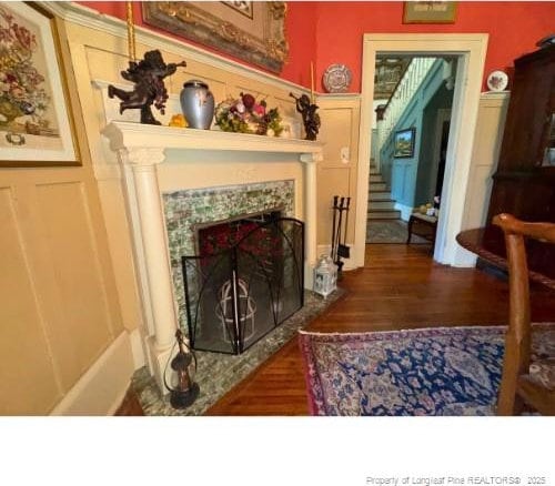 living area featuring a fireplace, stairway, a decorative wall, and wood finished floors