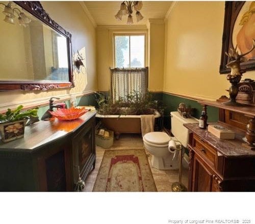 bathroom featuring a wainscoted wall, crown molding, vanity, and toilet