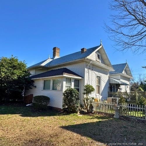 view of side of property featuring a chimney, fence, and a lawn