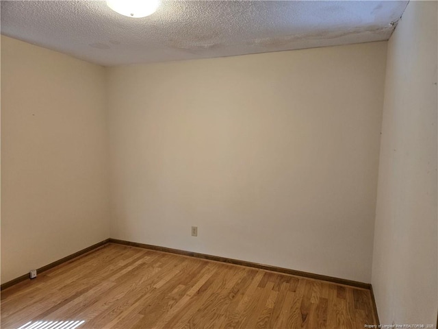 empty room featuring a textured ceiling, light wood-type flooring, and baseboards