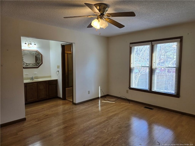 unfurnished bedroom with a textured ceiling, ensuite bathroom, wood finished floors, a sink, and baseboards