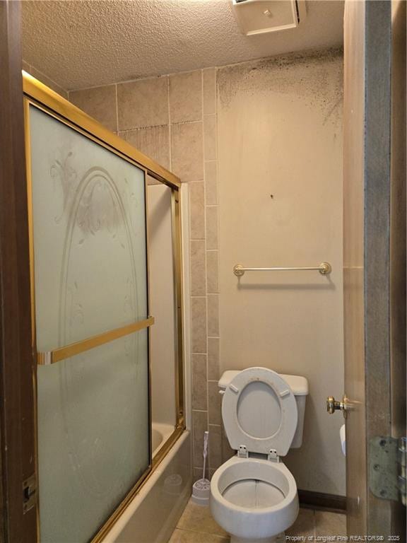 full bath with combined bath / shower with glass door, a textured ceiling, toilet, and tile patterned floors