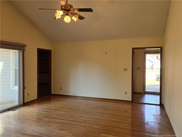 empty room with wood finished floors, visible vents, baseboards, vaulted ceiling, and a ceiling fan