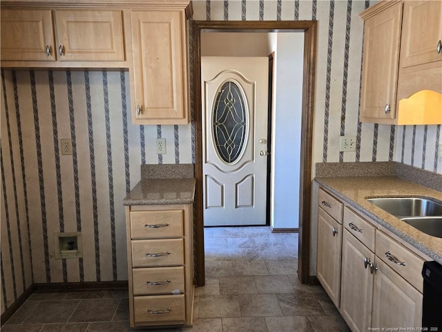 kitchen featuring wallpapered walls, black dishwasher, light brown cabinets, and a sink