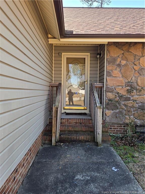 view of exterior entry featuring a shingled roof