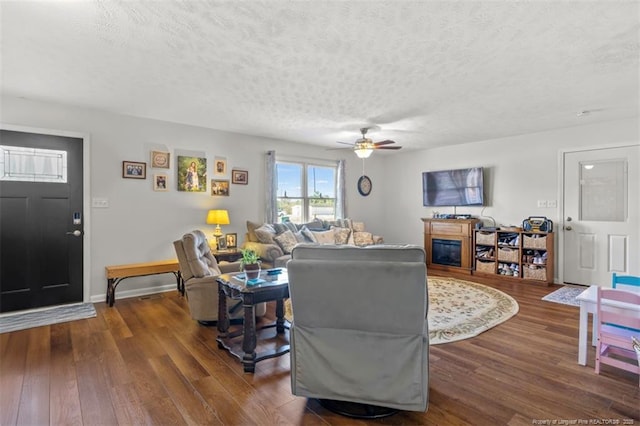 living area with a textured ceiling, ceiling fan, dark wood-style flooring, and baseboards