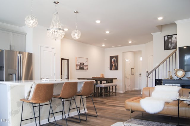 kitchen with dark wood finished floors, a kitchen breakfast bar, stainless steel refrigerator with ice dispenser, and ornamental molding