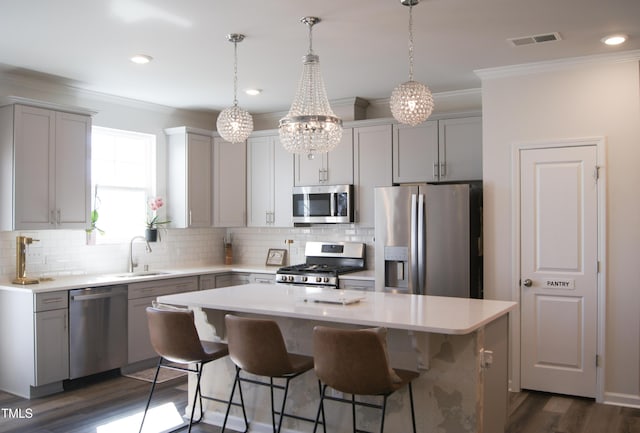 kitchen featuring visible vents, a sink, a kitchen island, stainless steel appliances, and crown molding