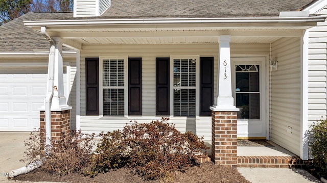 doorway to property with a porch, roof with shingles, and an attached garage