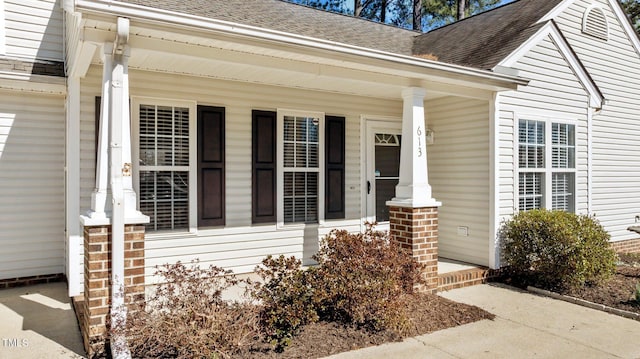 doorway to property with covered porch, a shingled roof, and brick siding