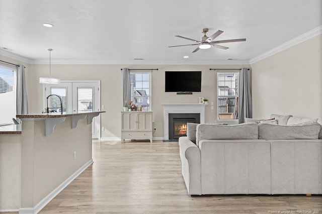 living area featuring a fireplace with flush hearth, a healthy amount of sunlight, ornamental molding, and light wood-style flooring