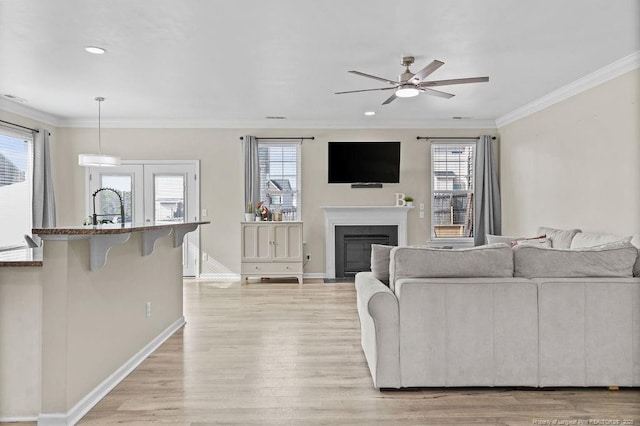 living room featuring light wood-style floors, crown molding, plenty of natural light, and a fireplace with flush hearth