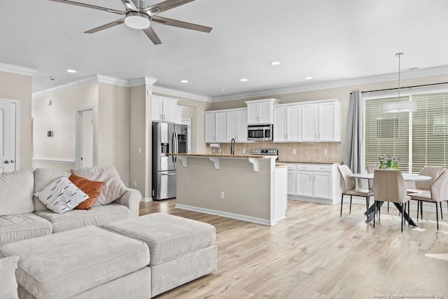 living area with recessed lighting, light wood-style floors, ornamental molding, ceiling fan, and baseboards