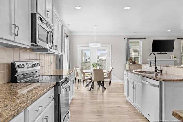 kitchen featuring decorative backsplash, light wood-style flooring, appliances with stainless steel finishes, ornamental molding, and a sink