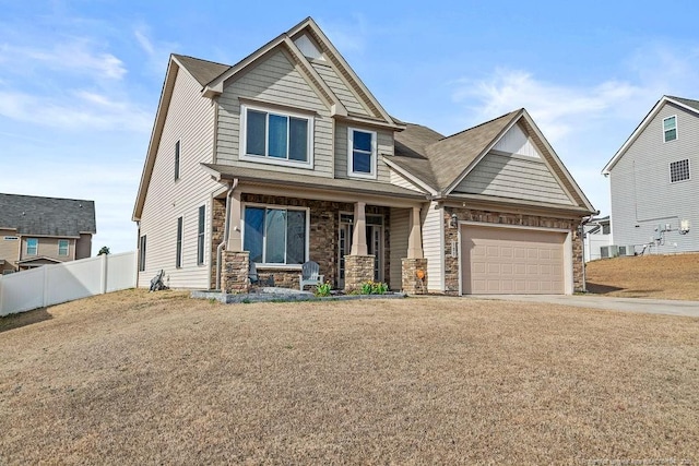 craftsman inspired home with a porch, an attached garage, fence, driveway, and stone siding