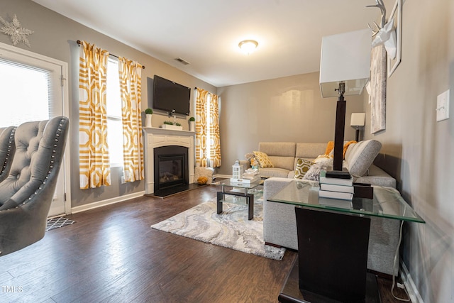 living area with a glass covered fireplace, visible vents, baseboards, and wood finished floors