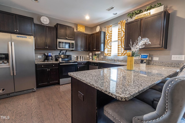 kitchen featuring stainless steel appliances, visible vents, a peninsula, and light stone countertops