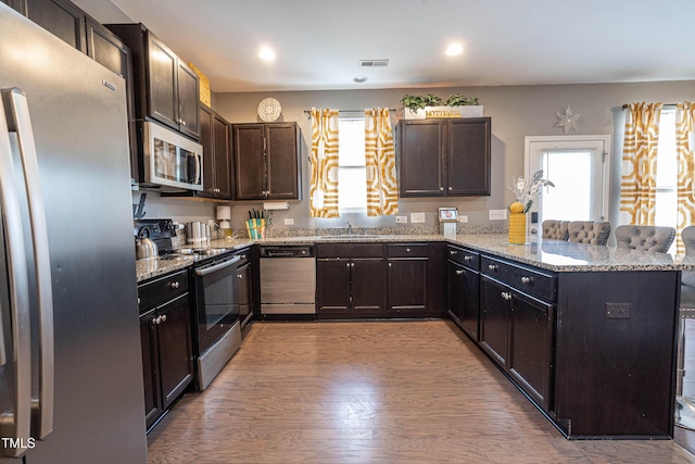 kitchen featuring dark brown cabinetry, visible vents, a peninsula, light stone countertops, and stainless steel appliances