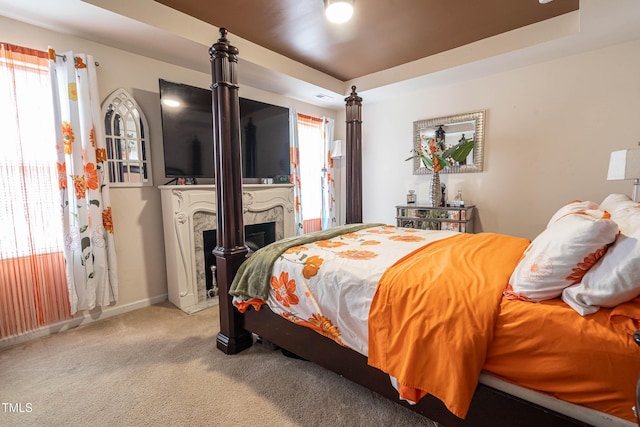 carpeted bedroom featuring baseboards, a fireplace, a tray ceiling, and multiple windows