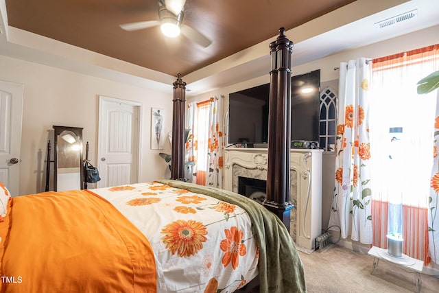 bedroom featuring a high end fireplace, a tray ceiling, visible vents, and carpet flooring