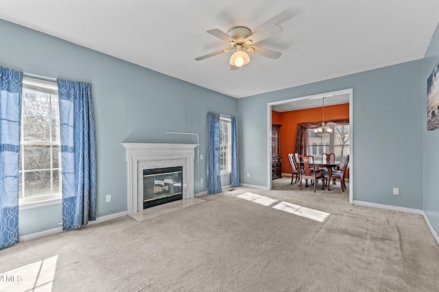 unfurnished living room featuring ceiling fan with notable chandelier, carpet flooring, baseboards, and a premium fireplace