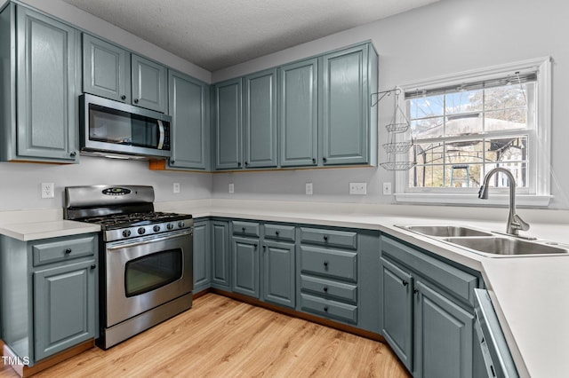 kitchen with light wood-type flooring, stainless steel appliances, a sink, and light countertops