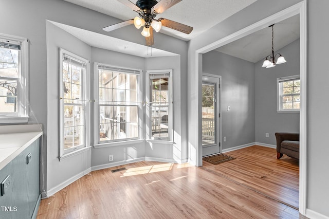 unfurnished dining area featuring baseboards, visible vents, vaulted ceiling, light wood-style floors, and ceiling fan with notable chandelier