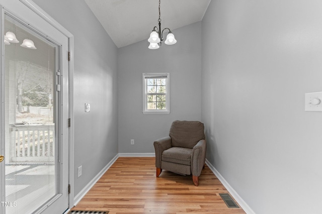 living area featuring lofted ceiling, a chandelier, light wood-style flooring, visible vents, and baseboards