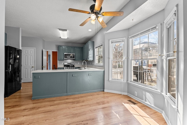 kitchen with gas range oven, stainless steel microwave, light wood-style floors, a peninsula, and black fridge