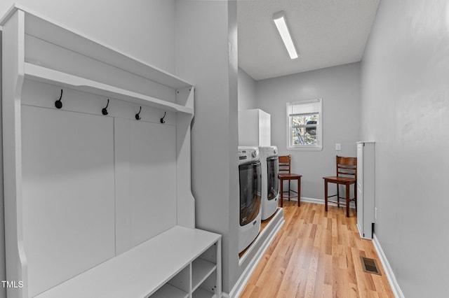 mudroom featuring light wood-style floors, washing machine and dryer, visible vents, and baseboards