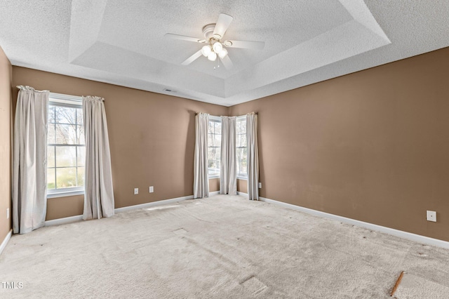 spare room with carpet floors, a tray ceiling, and baseboards