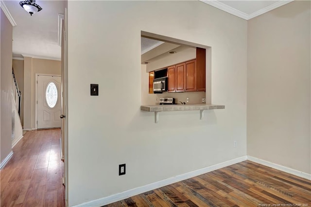 kitchen with light countertops, stainless steel microwave, brown cabinetry, ornamental molding, and wood finished floors