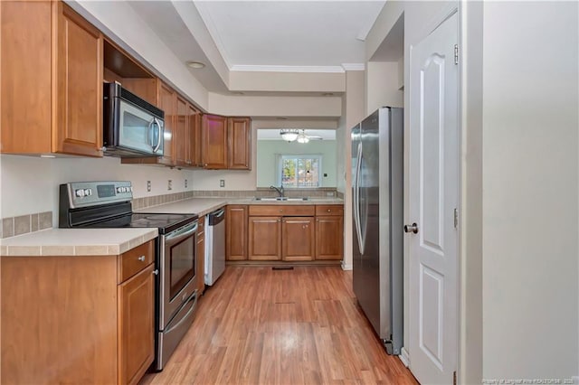 kitchen with light wood-style flooring, stainless steel appliances, light countertops, ornamental molding, and brown cabinetry