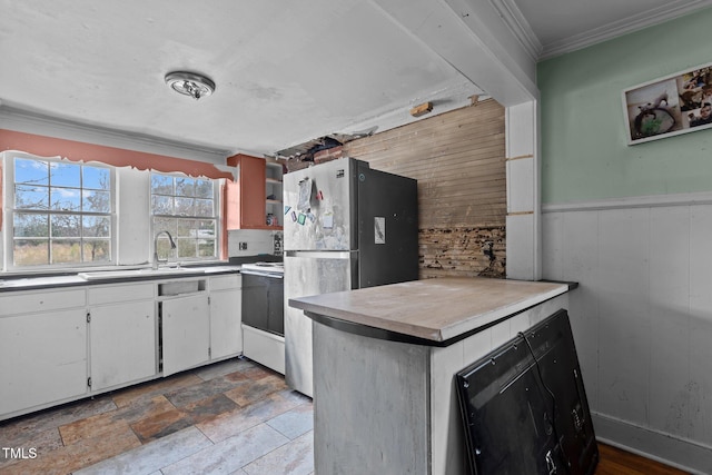 kitchen with a wainscoted wall, a sink, wooden walls, white cabinets, and crown molding