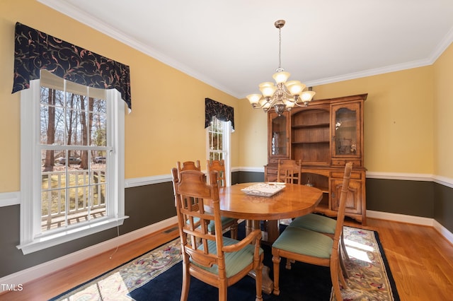 dining area featuring light wood-style flooring, crown molding, baseboards, and a notable chandelier