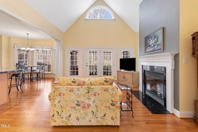 living room featuring baseboards, a tile fireplace, light wood-style floors, high vaulted ceiling, and a notable chandelier