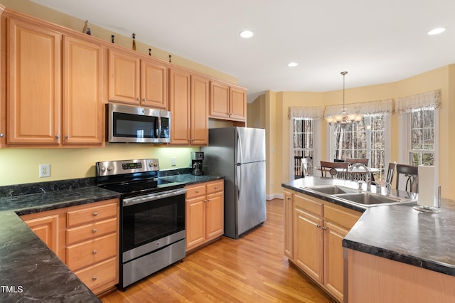 kitchen with appliances with stainless steel finishes, dark countertops, a sink, and light wood finished floors