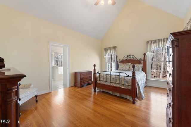 bedroom with baseboards, a ceiling fan, light wood-style flooring, ensuite bathroom, and high vaulted ceiling