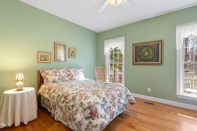 bedroom with ceiling fan, wood finished floors, visible vents, and baseboards