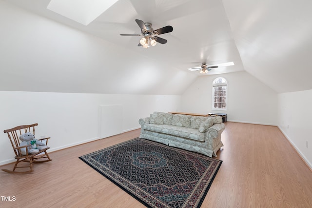 living area featuring vaulted ceiling with skylight, ceiling fan, baseboards, and wood finished floors