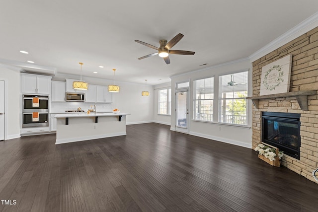 unfurnished living room with dark wood-type flooring, ornamental molding, a stone fireplace, a ceiling fan, and a sink