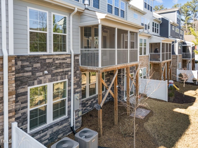 rear view of property with a sunroom, fence, stone siding, and central AC