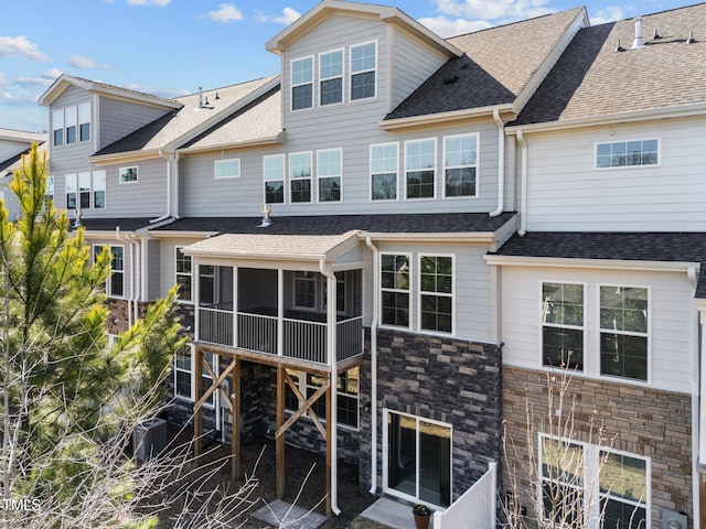 rear view of property featuring stone siding, a shingled roof, and a sunroom