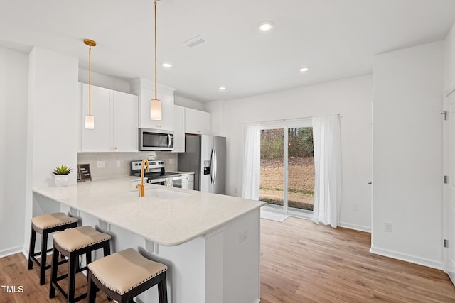 kitchen featuring light wood-style flooring, stainless steel appliances, light countertops, a kitchen bar, and backsplash