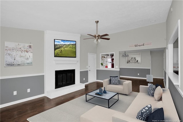 living room with ceiling fan, a brick fireplace, wood finished floors, and baseboards