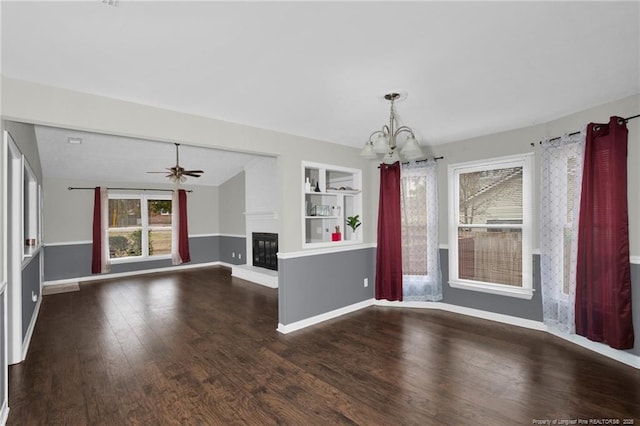 interior space featuring built in features, a fireplace, wood finished floors, baseboards, and ceiling fan with notable chandelier