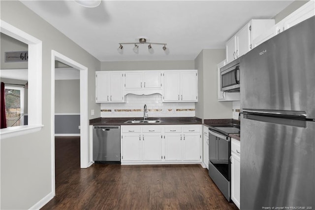 kitchen with appliances with stainless steel finishes, dark countertops, white cabinets, and a sink