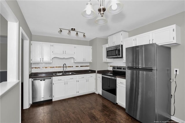 kitchen with stainless steel appliances, dark countertops, dark wood-type flooring, white cabinets, and a sink